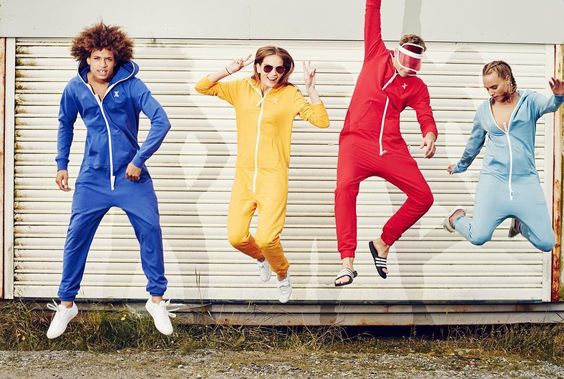 Vier Models in blauem, gelbem, rotem und hellblauem Jumpsuite hüpfend